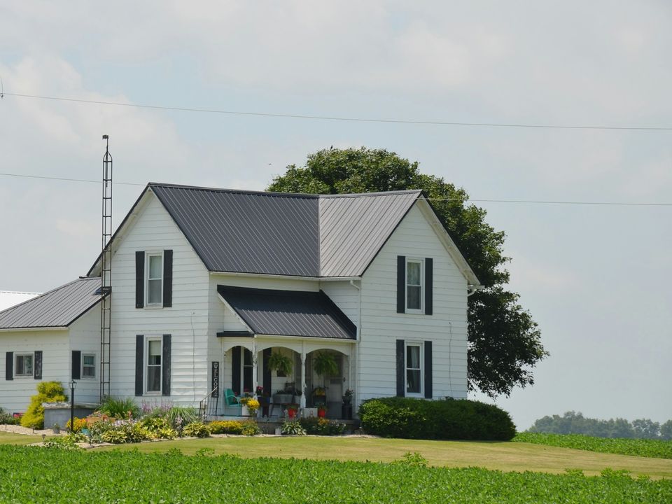 White two-story farmhouse with dark shutters and a mown lawn