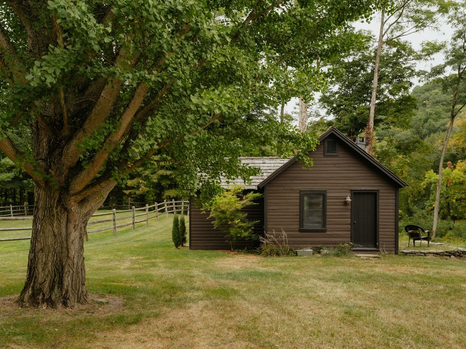 Small wooden house with a grass yard and a large tree in rural New York