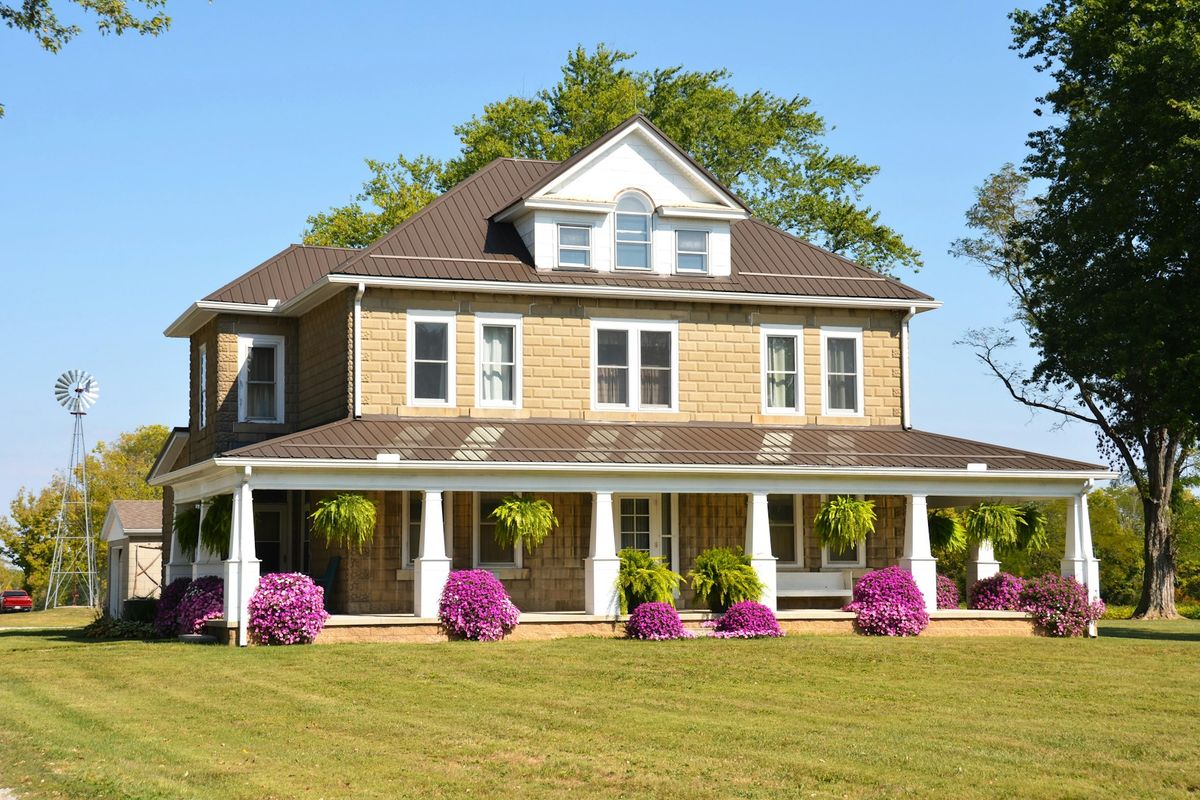 Two-story farmhouse with a wraparound porch and a water-pumping windmill